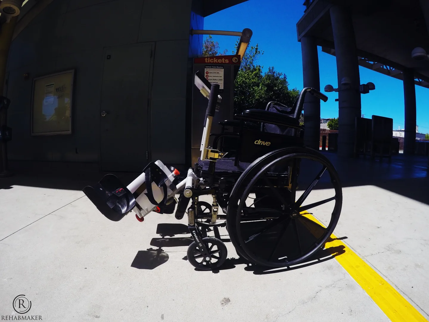 Side view of the LegMaker prototype attached to a manual wheelchair at a transit station